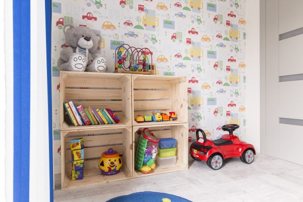 A children's room with tools displayed, like a car to ride with, a teddy bear, puzzles etc. The wall is a playful print Grafiprint Wall deco PVC-free
