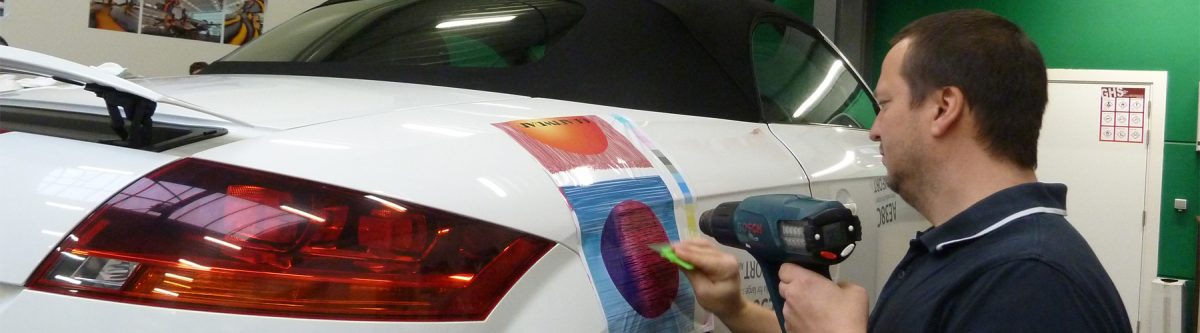 Cursist neemt deel aan een van de Grafityp-trainingen en kleeft een folie op een witte auto
